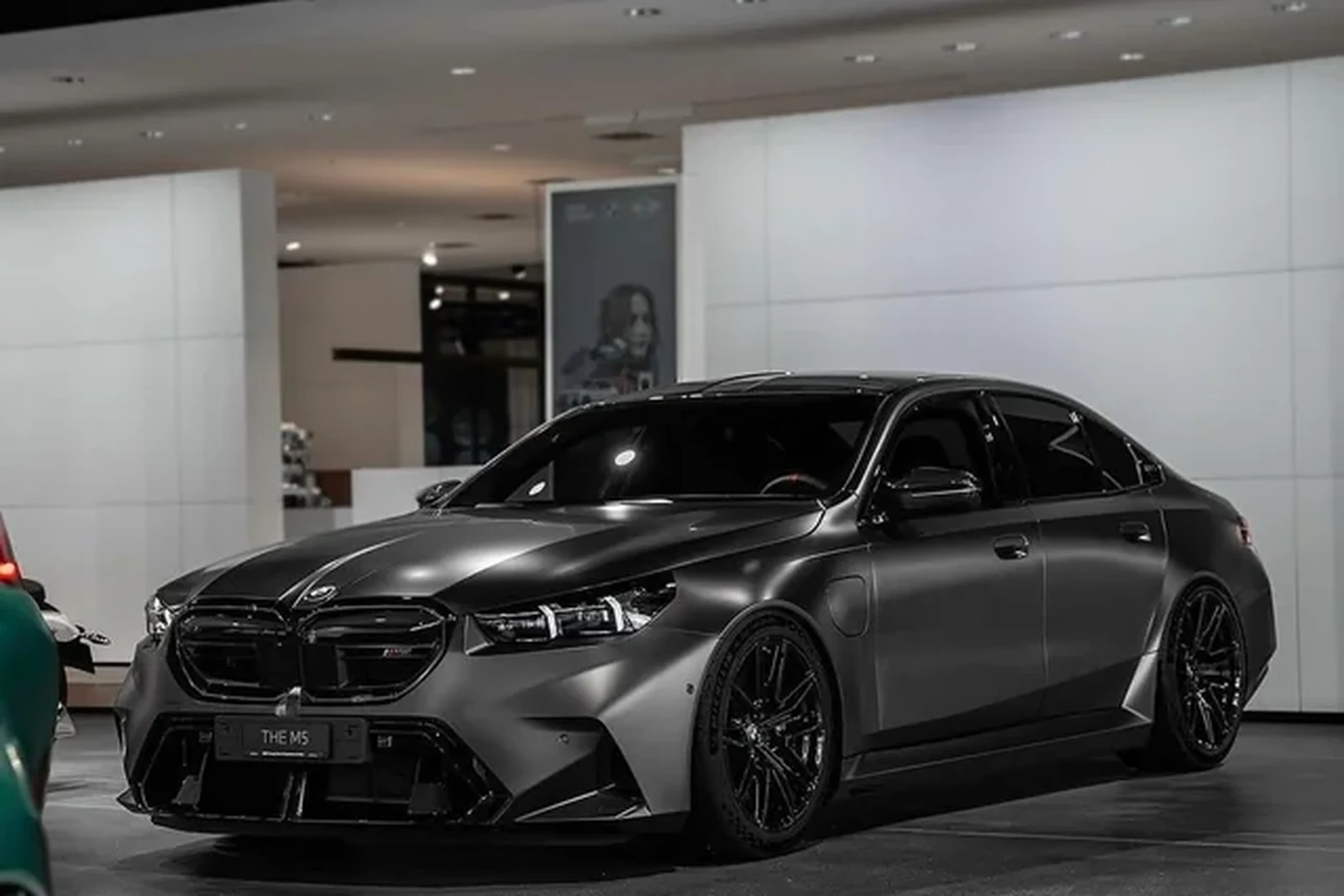 Dark grey BMW G90 M5 sedan on a showroom floor with black wheels
